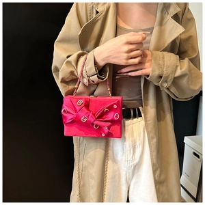 Detail of rose red silk evening clutch featuring rhinestone bow and metal handle