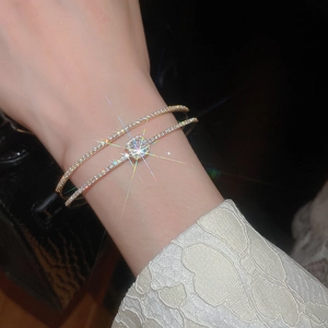 Detail of a double-layer gold bangle with zircon bow and square stone on a model's wrist
