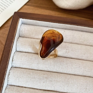 Gros plan d'une bague ovale en résine ambre avec anneau doré dans un écrin beige