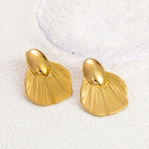 Macro view of gold plated fan-shaped titanium earrings with radial textures on white fabric