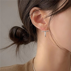 Close-up of minimalist sterling silver T-shaped stud earring worn on earlobe for styling