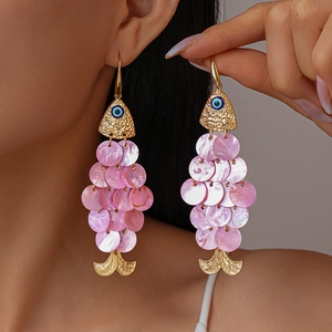Close-up of pink shell fish earrings with blue eye detail and gold-tone fringe