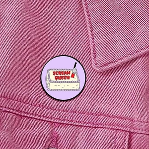 Detailed close-up of a Scream Queen horror movie pin on a pink denim jacket