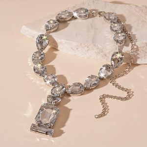 Luxurious silver necklace with teardrop and square crystals on a textured stone surface