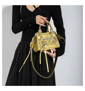 Close-up of metallic gold handbag with rivets, heart mirror, and tassel details on model
