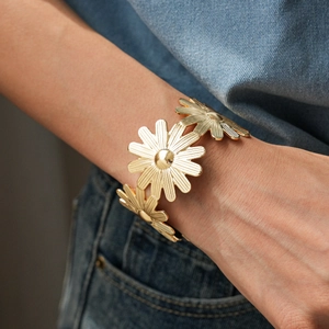 Gros plan d'un bracelet ouvert à fleurs de marguerite dorées porté sur le bras avec jean