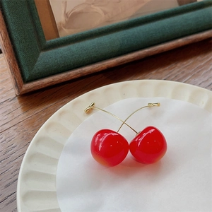 Cute red cherry earrings with gold stems displayed on a stylish cream jewelry dish