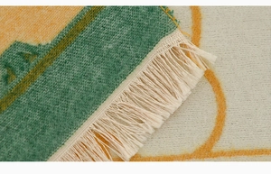 Close-up of the woven textile rug featuring green patterns and cream fringe details