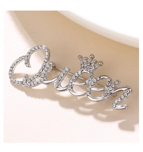 Detailed view of silver Queen brooch with sparkling rhinestones and crown emblem