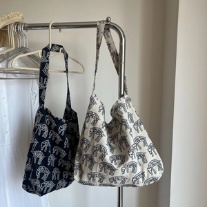Close-up of canvas tote bags with hand-drawn sheep patterns on a wooden hanger