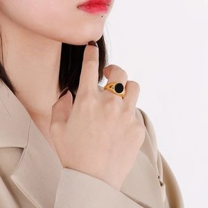 Close-up of minimalist gold-plated signet ring with black circular inlay on a model hand