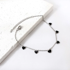 Minimalist silver stainless steel anklet with black heart pendant on a stone background