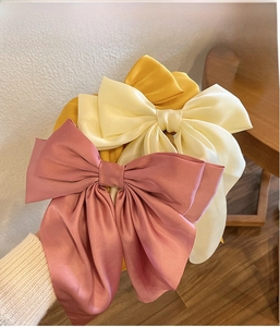 Detail of glossy satin bow headband showing fine pleats and silky fabric texture
