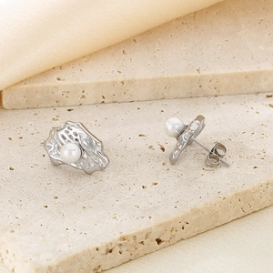 Detail of irregular textured silver earrings with center white pearl on a stone surface