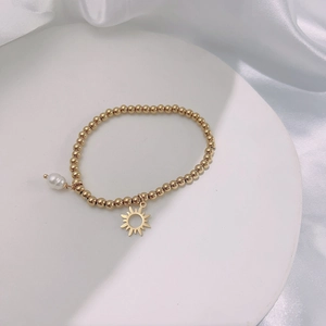 Close-up of golden beaded bracelet with pearl and sun charm on a ceramic display