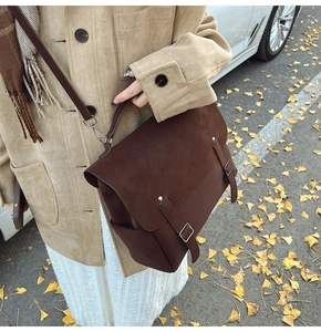 Detalle de bolso mensajero de ante marrón oscuro con doble hebilla decorativa para mujer