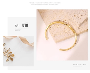 Dettaglio di un bracciale rigido a C placcato oro su uno sfondo di pietra beige naturale