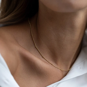 Detailed close-up of a delicate gold satellite chain necklace on a woman's neck.