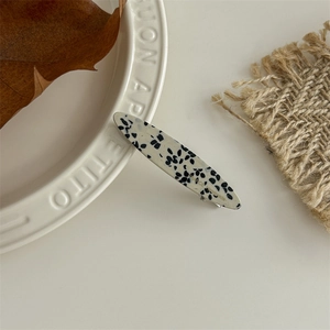 Detail of French tortoiseshell resin hair clip with gold logo on a warm minimal background