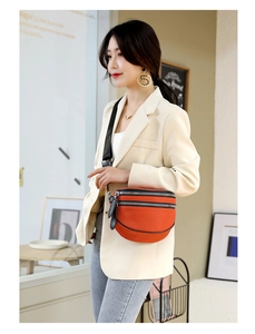 Detail of an orange crescent crossbody bag with black wide strap and multi-layer zippers