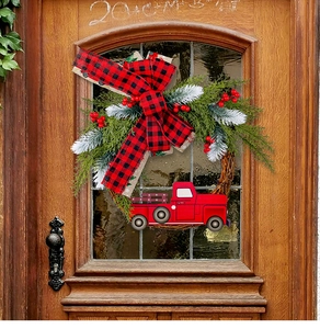 Detail eines Weihnachtskranzes mit rotem LKW, Karoschleife und Kiefernnadeln an Holztür