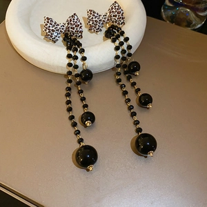 Close-up of leopard print bow earrings with elegant black beaded tassels and gold accents