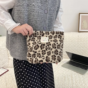 Detailed view of a plush leopard print makeup bag held against a cozy indoor background