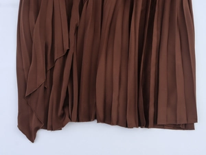 Detailed macro view of the brown pleated fabric and irregular hem of this elegant dress