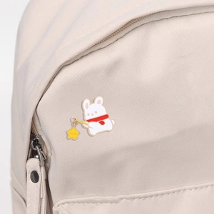 Detail of cute rabbit enamel pin with red scarf and yellow star on a beige backpack