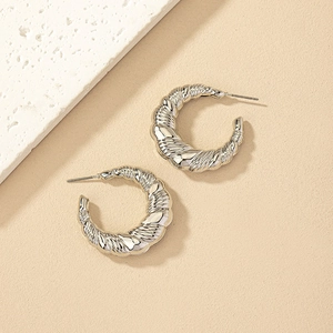 Chunky silver C-shaped croissant hoop earrings with spiral twist texture on beige stone