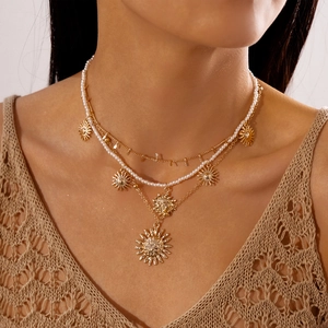 Close-up of triple-layered gold sun pendant necklace set with faux pearls on a model