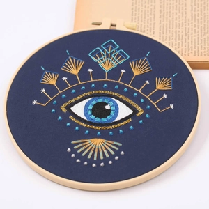 Completed evil eye embroidery kit in a wooden hoop with detailed blue and gold threadwork
