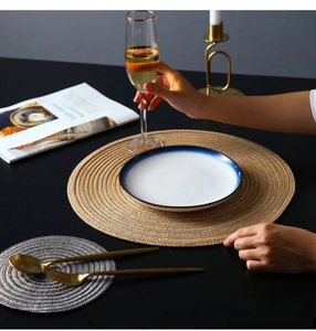 Detail of round woven table mats in beige and grey with plate and golden cutlery