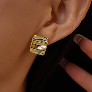 Macro shot of gold square stud earrings with irregular folded texture on model's ear