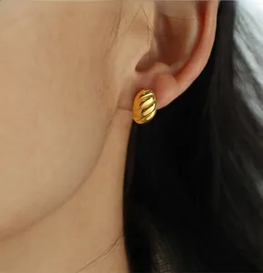 Close-up of a gold croissant hoop earring with spiral texture worn by a model