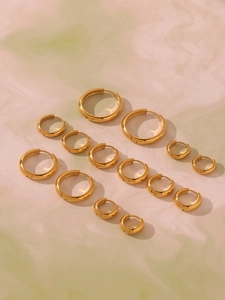 Multiple sizes of golden stainless steel hoop earrings arranged on a soft pastel background