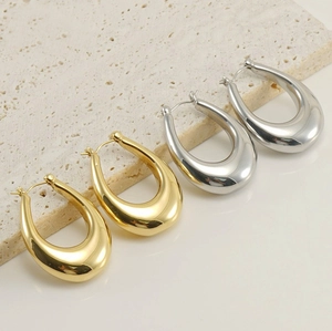 Polished gold and silver waterdrop hoop earrings displayed on a textured beige stone plate