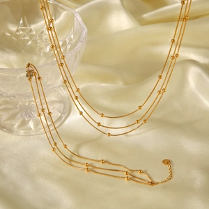 Detailed shot of layered gold titanium steel necklace with beads on silk fabric