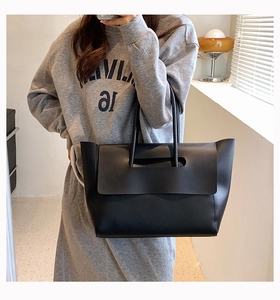 Detailed view of a black matte leather tote bag carried by a model in a modern office