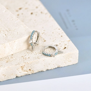 Close-up of silver spike hoop earrings with blue turquoise stones on stone prop
