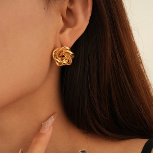 Close-up of golden metallic twisted flower stud earrings on a model's ear with high gloss