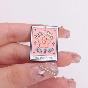Pink enamel brooch with flower and Taylor Swift lyrics held by hand with glitter nails