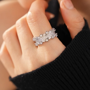 Close-up of a silver floral ring with cubic zirconia on a finger over a black sleeve