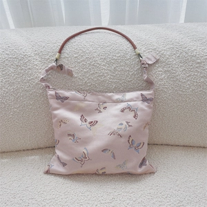 Close-up of pink jacquard butterfly shoulder bag with brown leather handle on a soft sofa