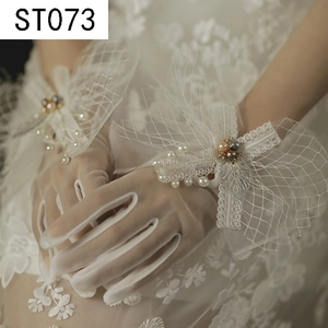Close-up of white lace bridal gloves with delicate pearls and silver leaf details