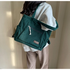 Close-up of dark green corduroy tote bag featuring a premium brown leather label detail