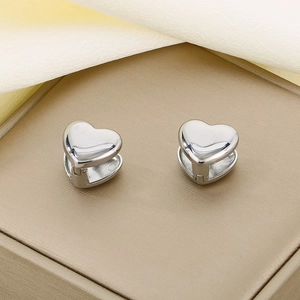 Detailed view of polished silver heart-shaped steel earrings on a textured jewelry box