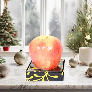 Realistic red apple shaped candle lit on a decorative base with festive background