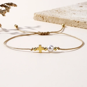 Detail of adjustable woven cord bracelet with gold cross charm and single pearl accent