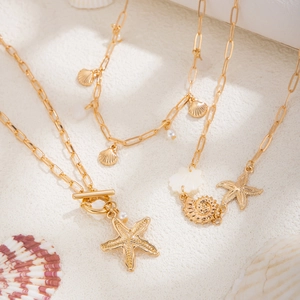 Close-up of golden starfish, seashell and conch charms on a long-link chain necklace